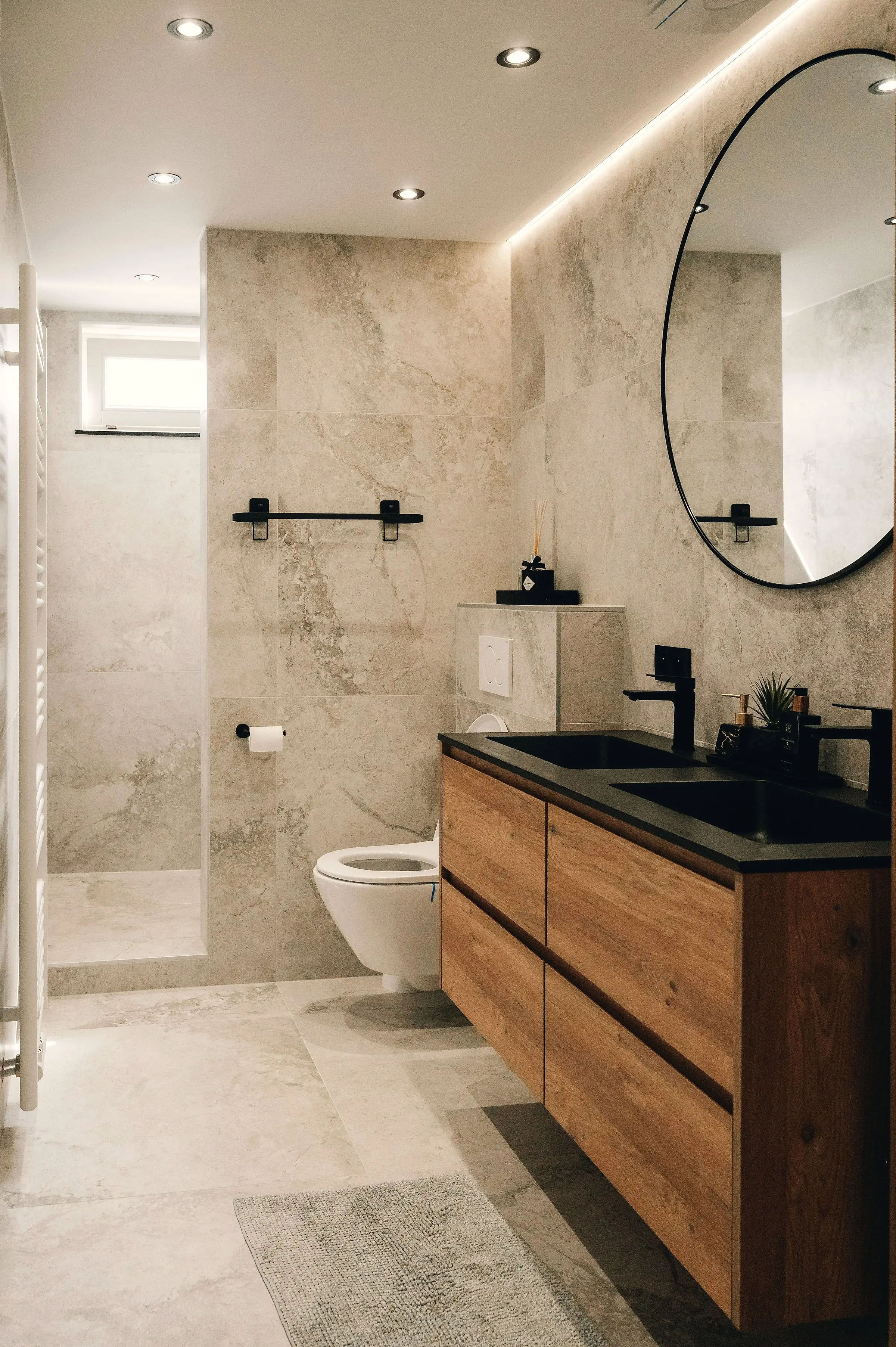 Baño reformado con revestimiento de travertino, mueble de madera y grifería negra